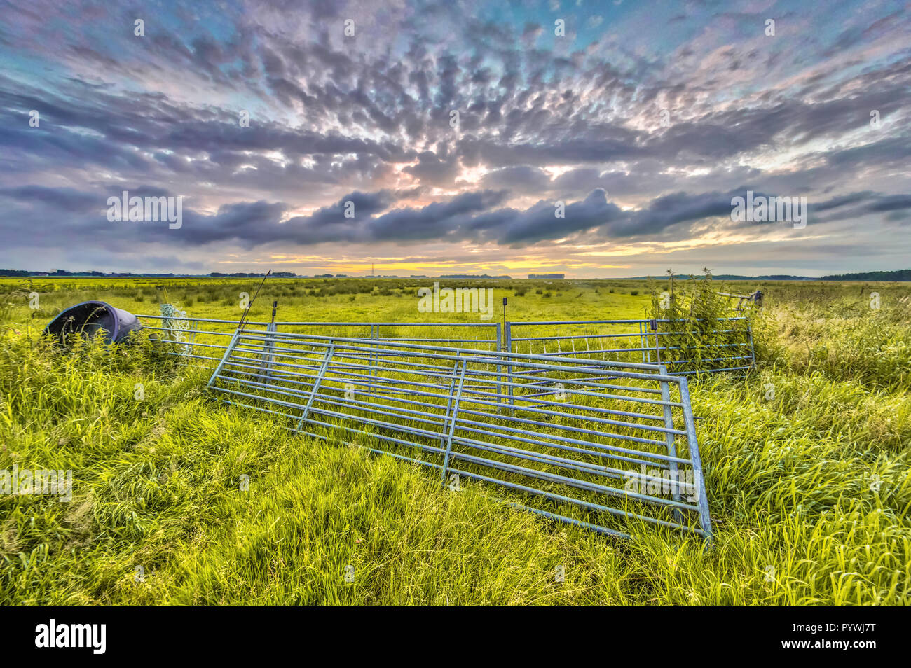 Metal gates in farmland field under setting sun with beautiful clouded sky Stock Photo