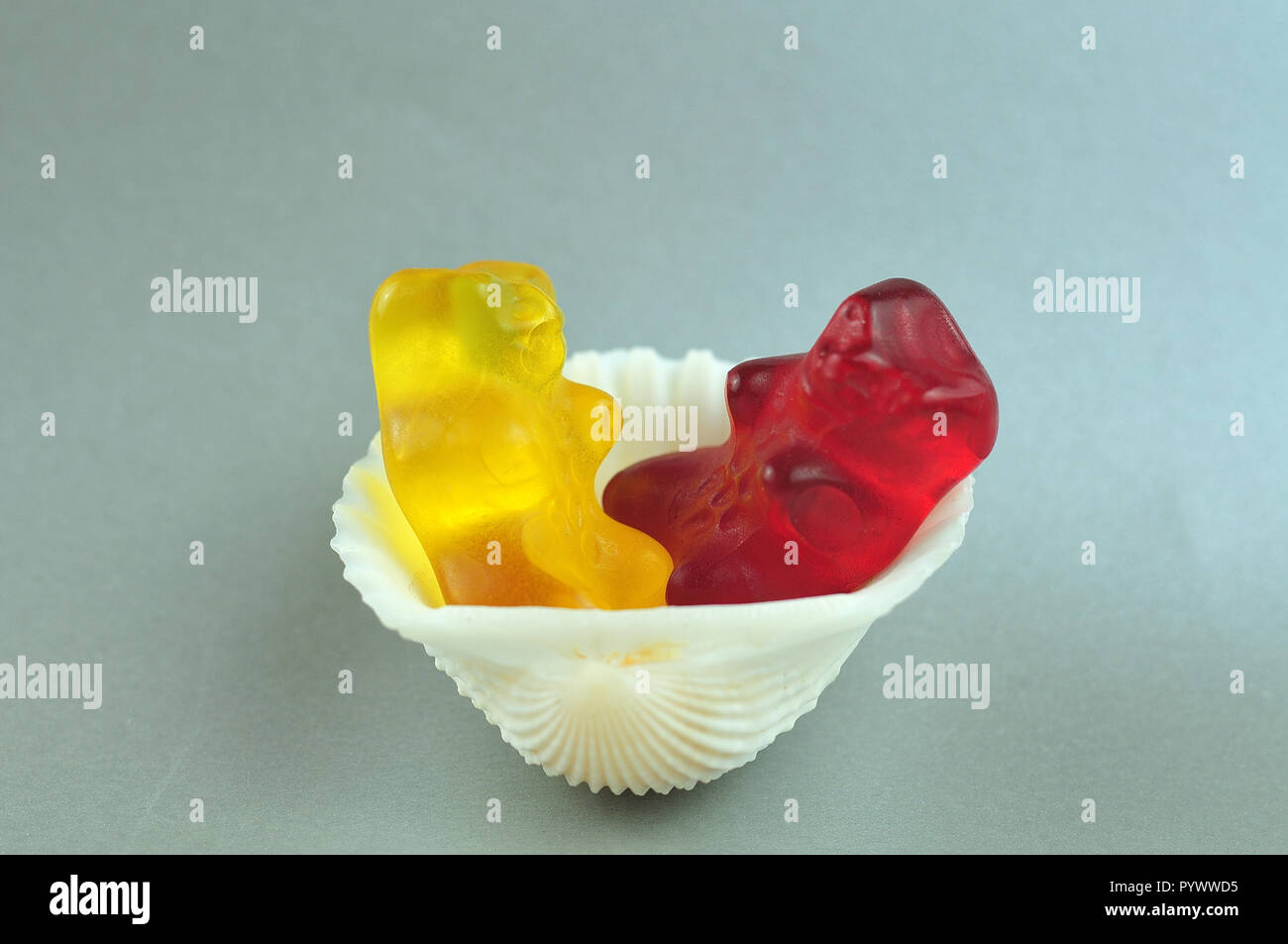 macrophotography of red and yellow gummy bear sitting in a white cockle shell Stock Photo