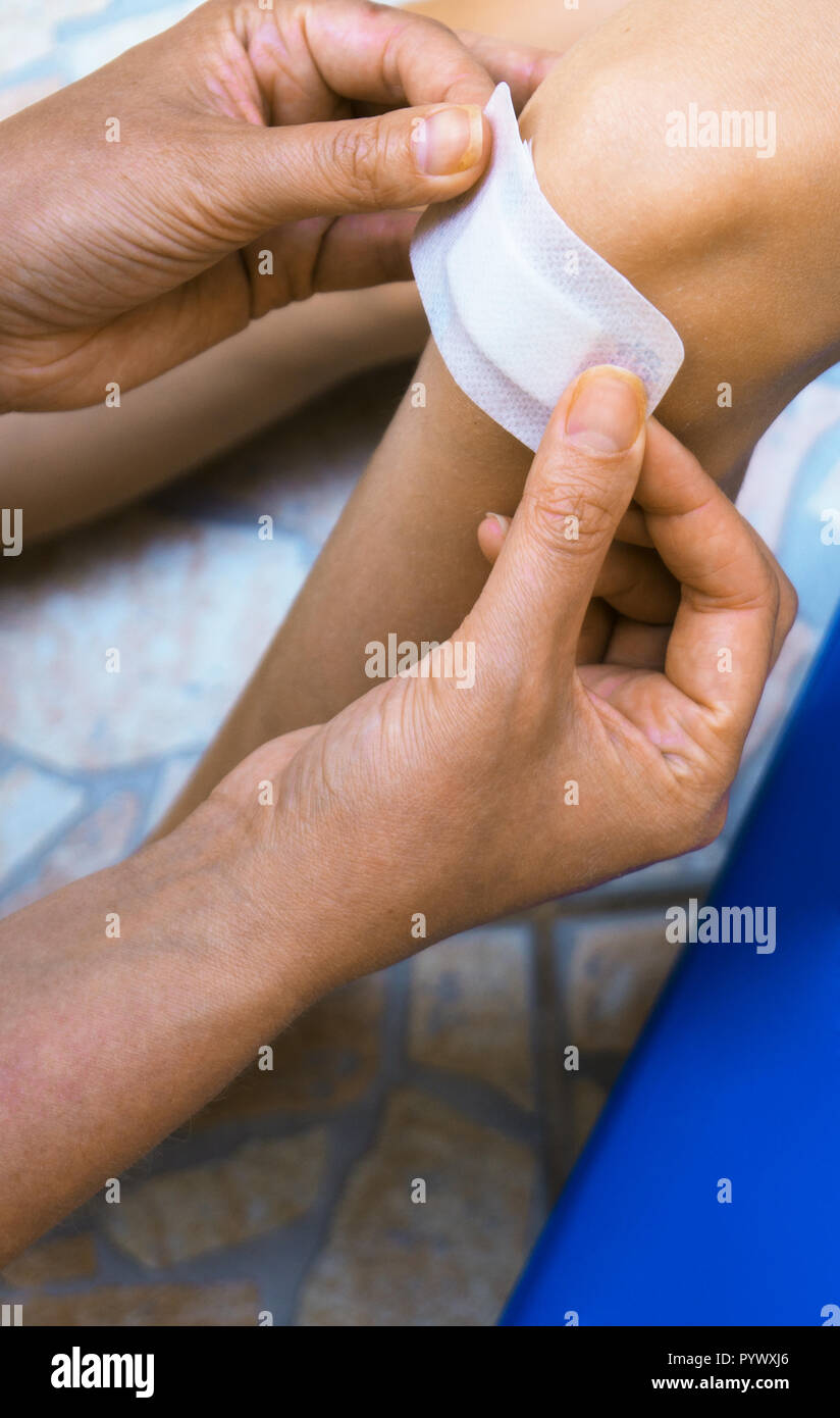 Woman puts adhesive bandage on child knee. Stock Photo