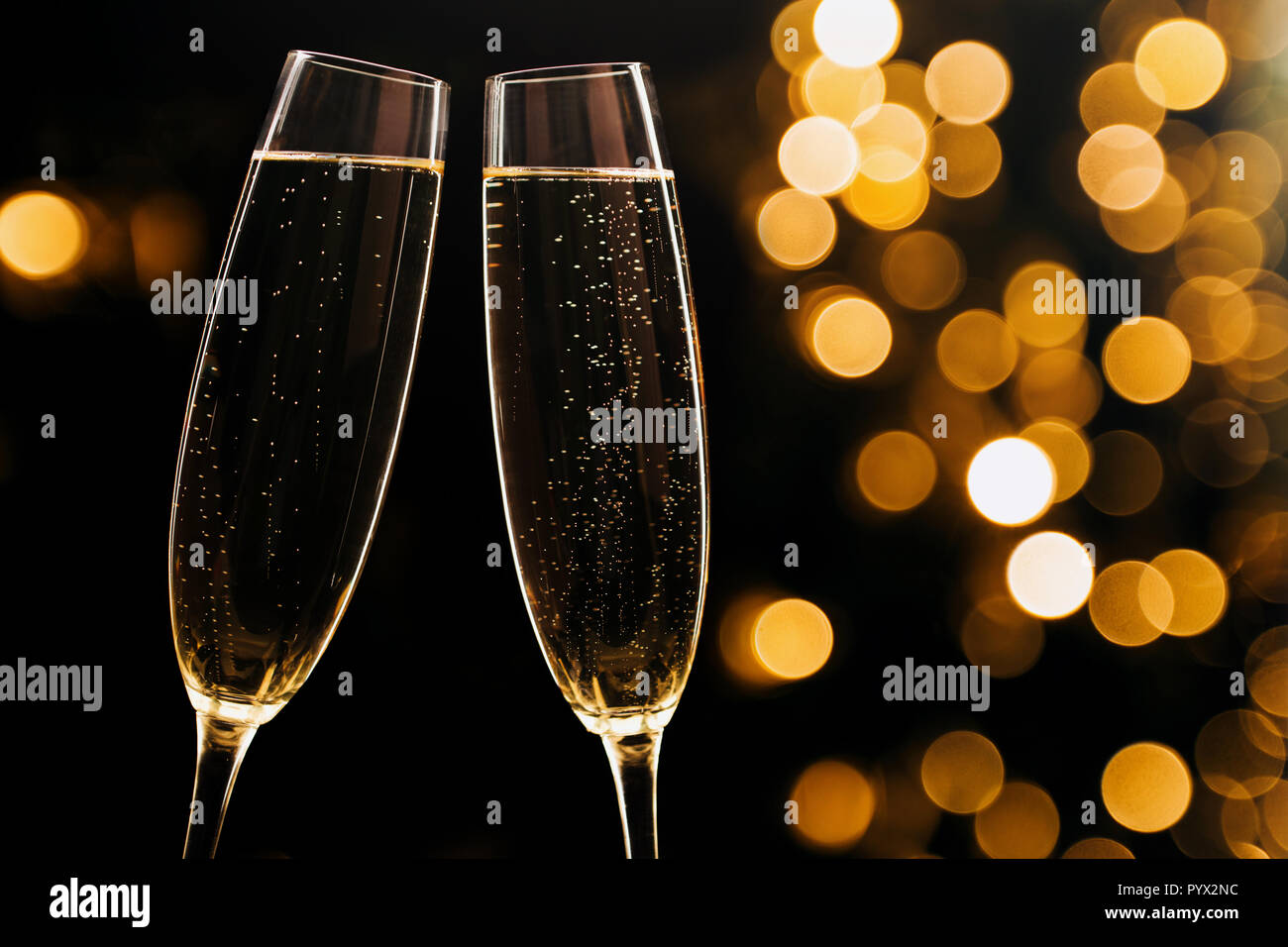 Two glasses of champagne on black stylish background with golden bokeh