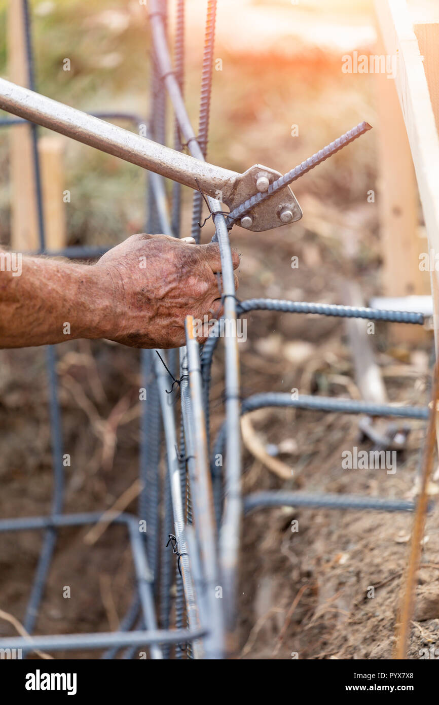 Worker Using Tools To Bend Steel Rebar At Construction Site. Stock Photo