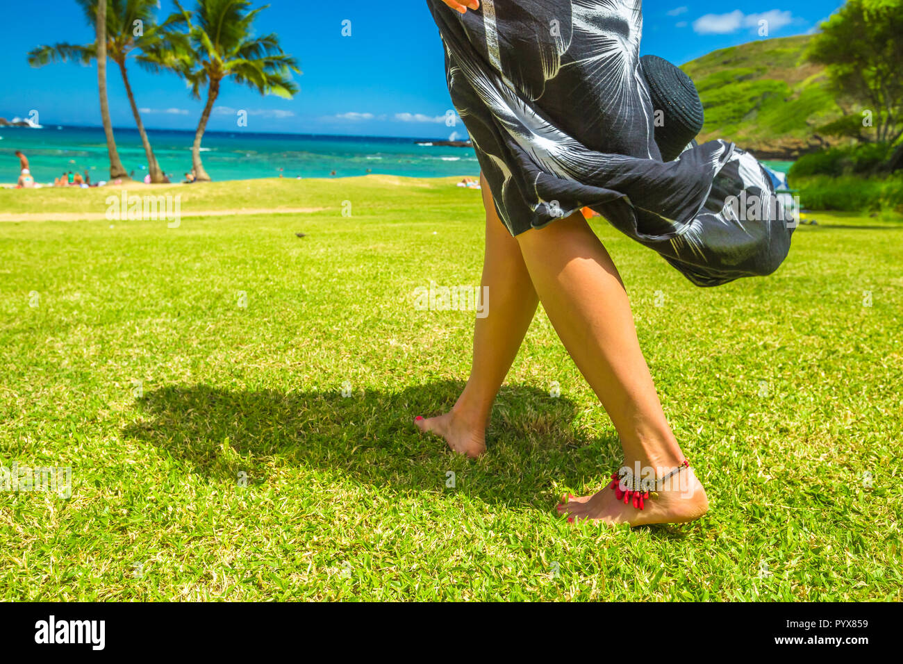 A woman walking barefoot with red anklet on Hanauma Bay Nature Preserve grass, Oahu, Hawaii, United States. Stock Photo