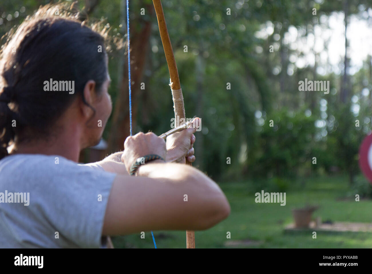 A male sport archer shooting an arrow with a bow at a red wooden target Stock Photo