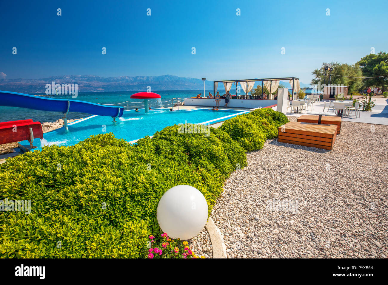 Pool with toboggan in holiday resort on Brac island with palm trees and turquoise clear ocean water, Supetar, Brac, Croatia Stock Photo