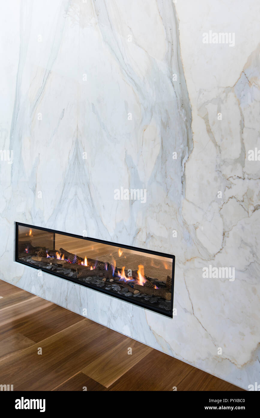 Gas fireplace integrated into marble wall provides a room divider allowing fire to be enjoyed from both sides in contemporary designed home Stock Photo