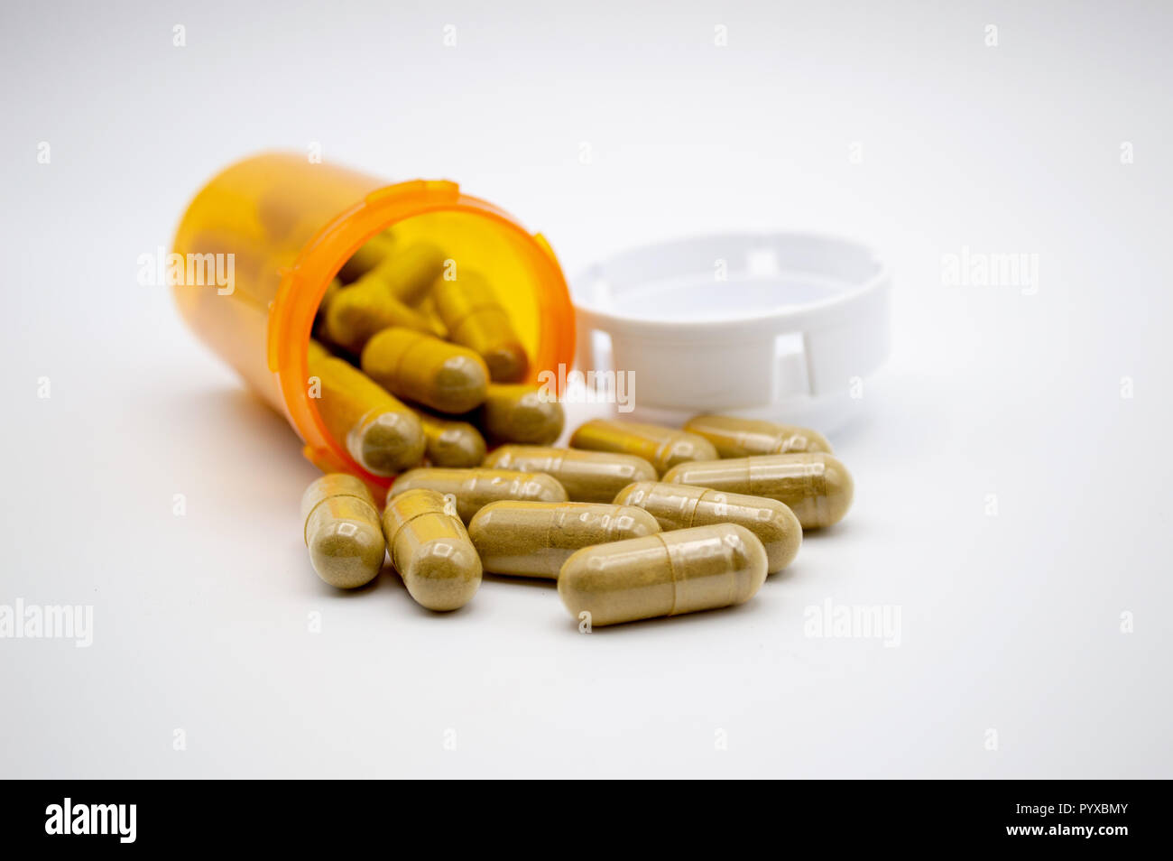 Green capsules of Kratom powder spilling out of an orange pill bottle with white cap onto a white background Stock Photo