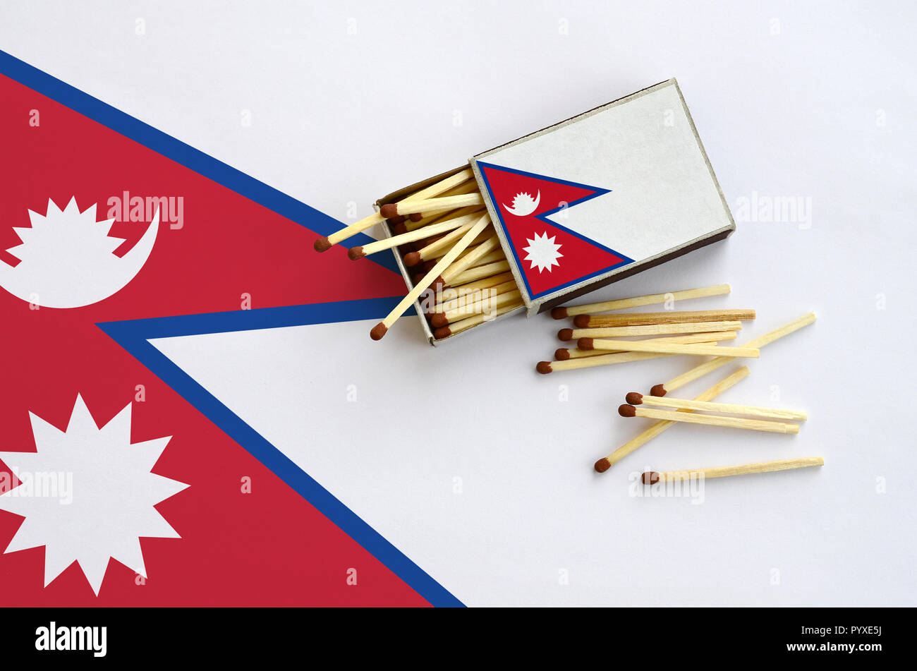 Nepal flag  is shown on an open matchbox, from which several matches fall and lies on a large flag. Stock Photo