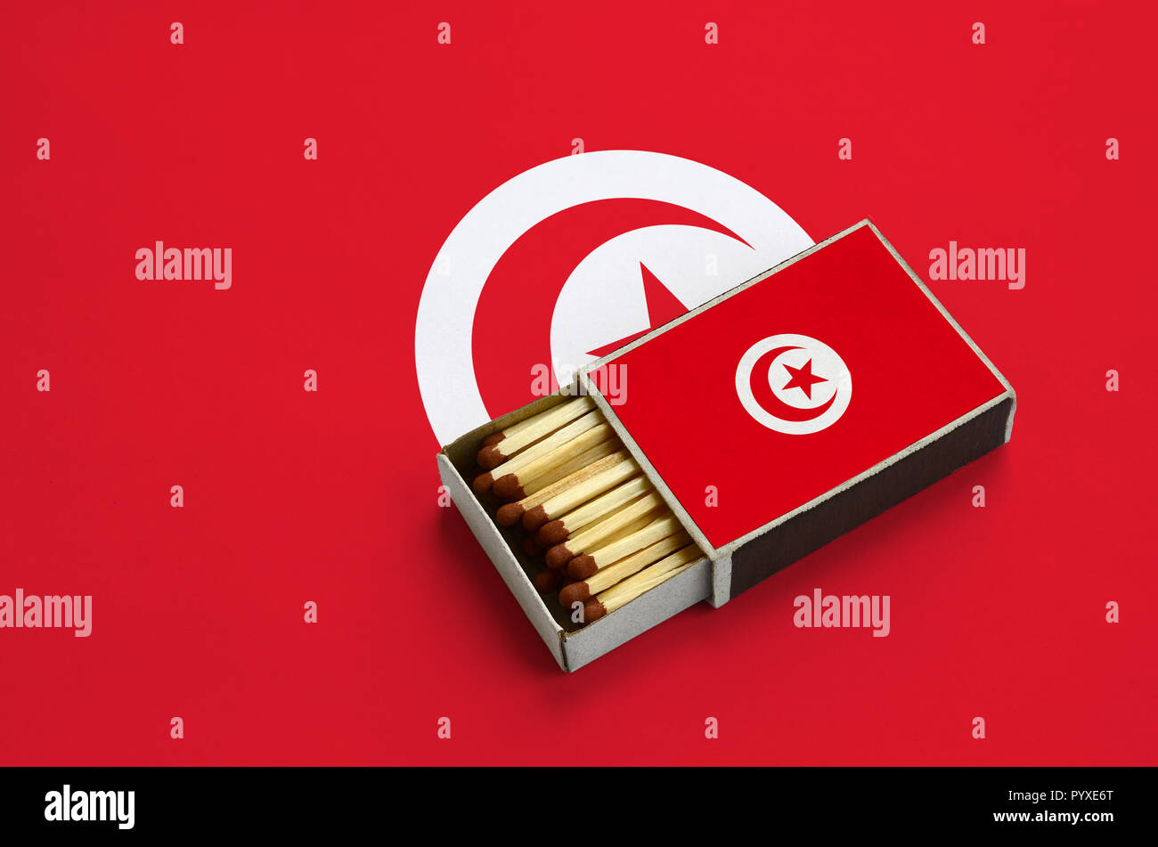 Tunisia flag  is shown in an open matchbox, which is filled with matches and lies on a large flag. Stock Photo