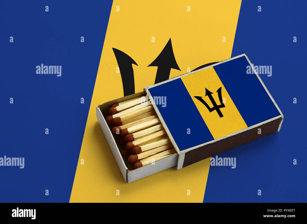 Barbados flag  is shown in an open matchbox, which is filled with matches and lies on a large flag. Stock Photo
