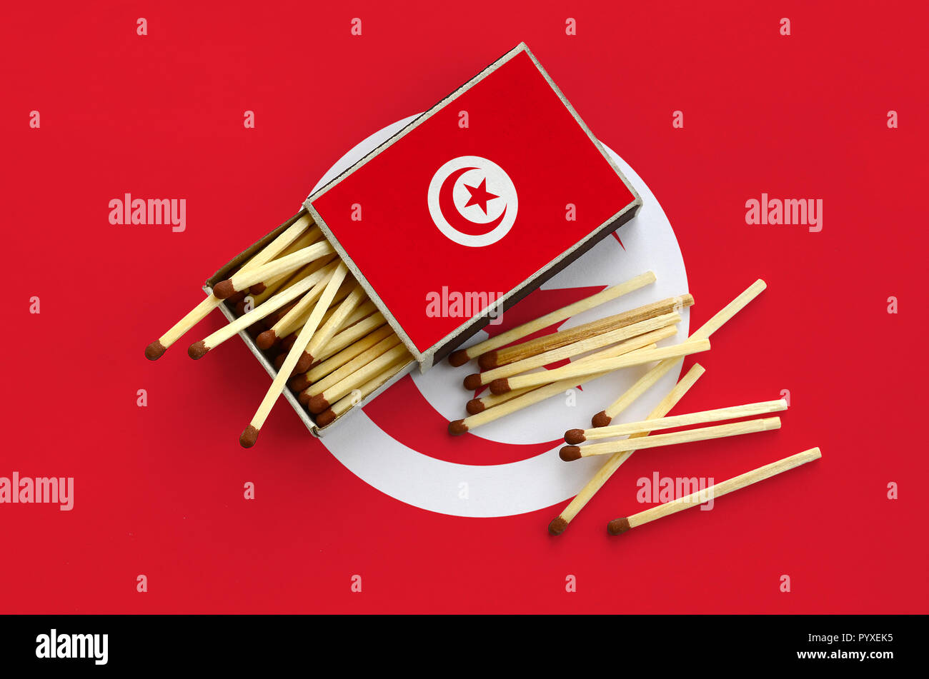Tunisia flag  is shown on an open matchbox, from which several matches fall and lies on a large flag. Stock Photo