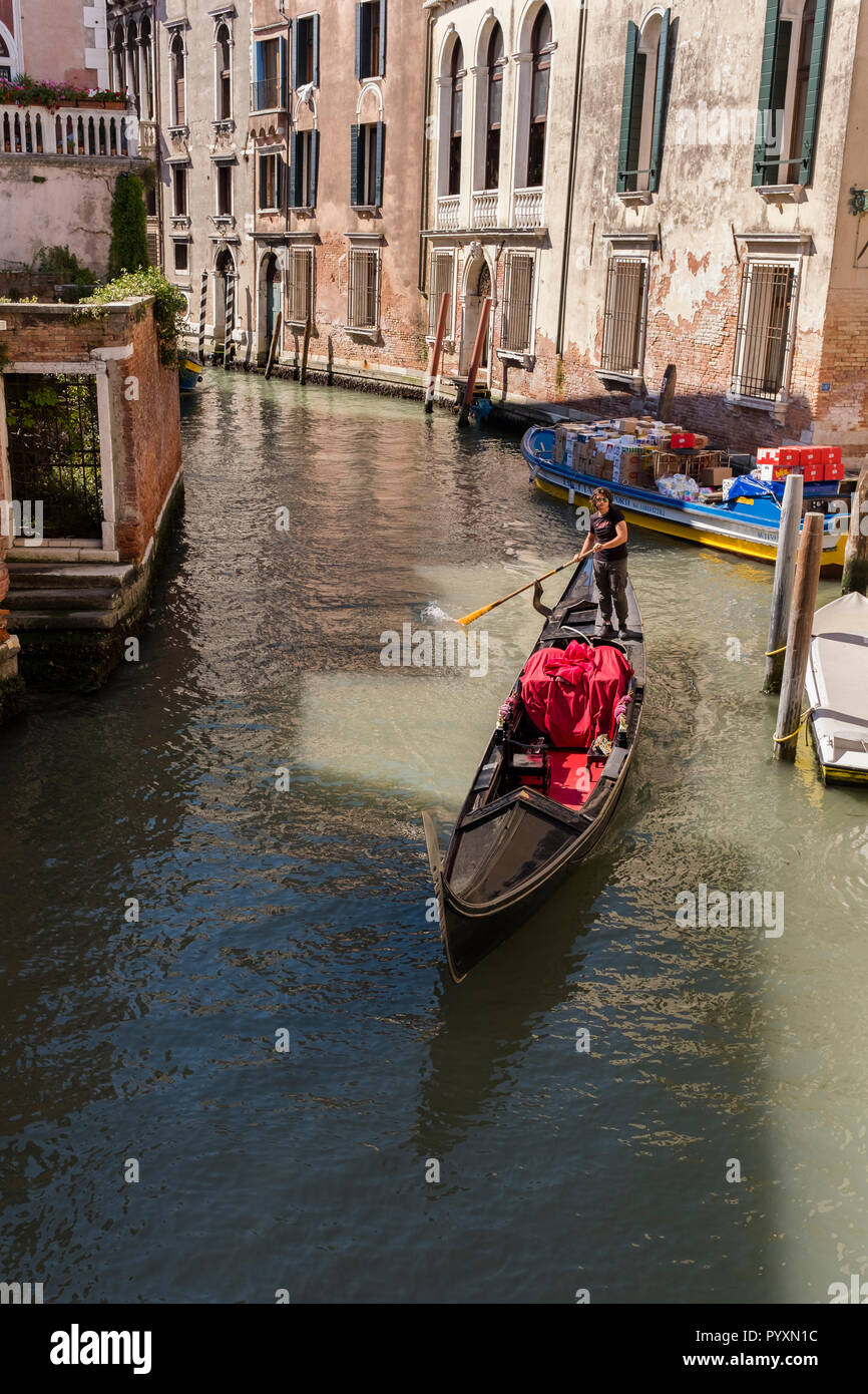 A gondola passes through a patch of sun on the water of a canal in ...