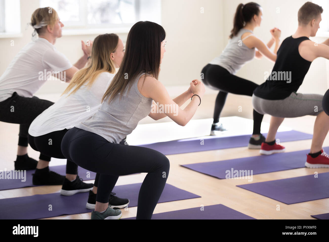 Sportive girls and guys doing crouching at gym Stock Photo