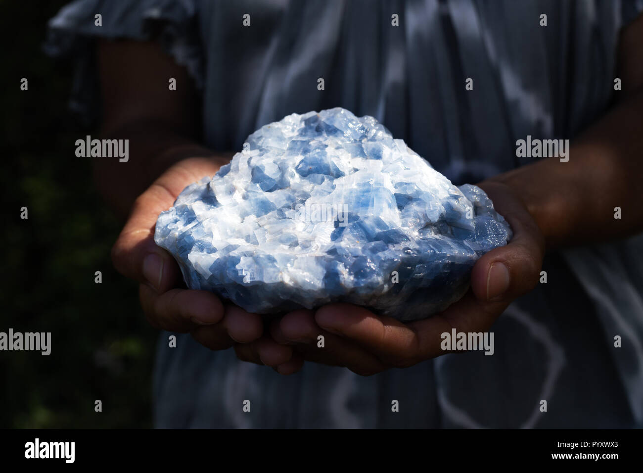 Close up of a woman holding a powerful healing blue calcite crystal in her hands in dark, moody light. Stock Photo