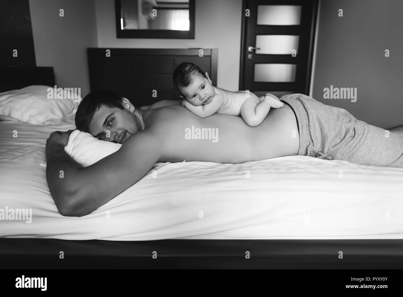 black and white picture of infant boy laying on father back in bed at home Stock Photo