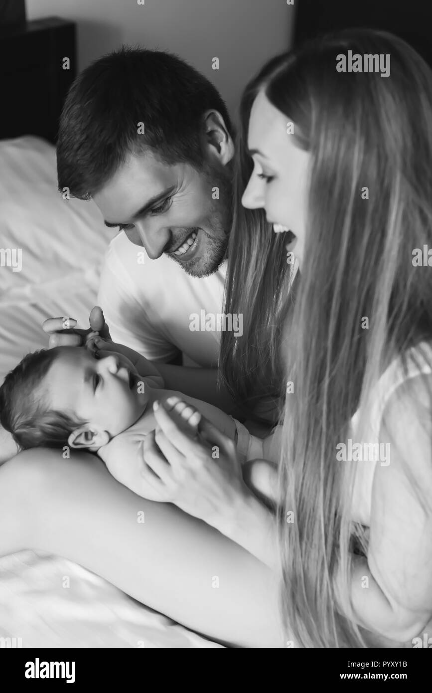 black and white picture of happy family playing with infant son in bed