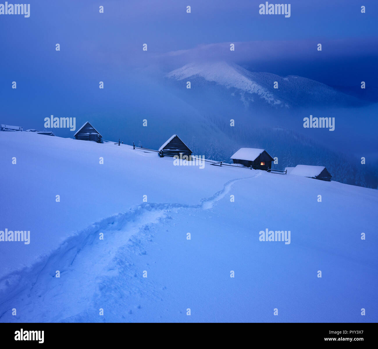 Winter landscape with mountain huts and a footpath in the snow. Blue twilight Stock Photo