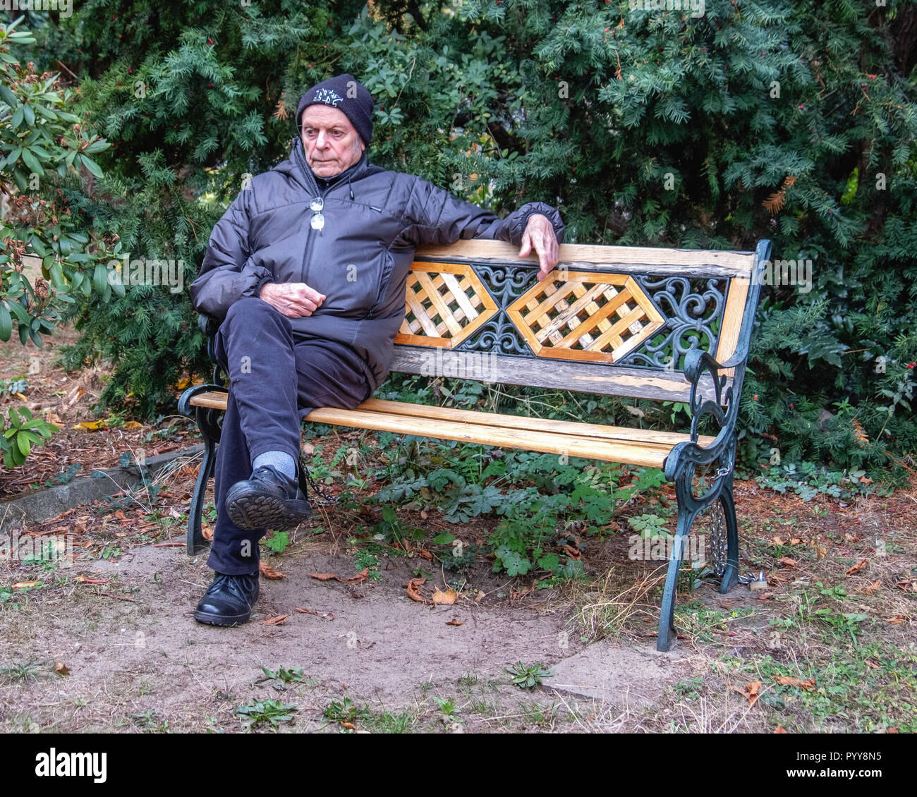 Senior man sitting on decorative wrought iron & wood bench, looking pensive,thoughtful, sad. Stock Photo