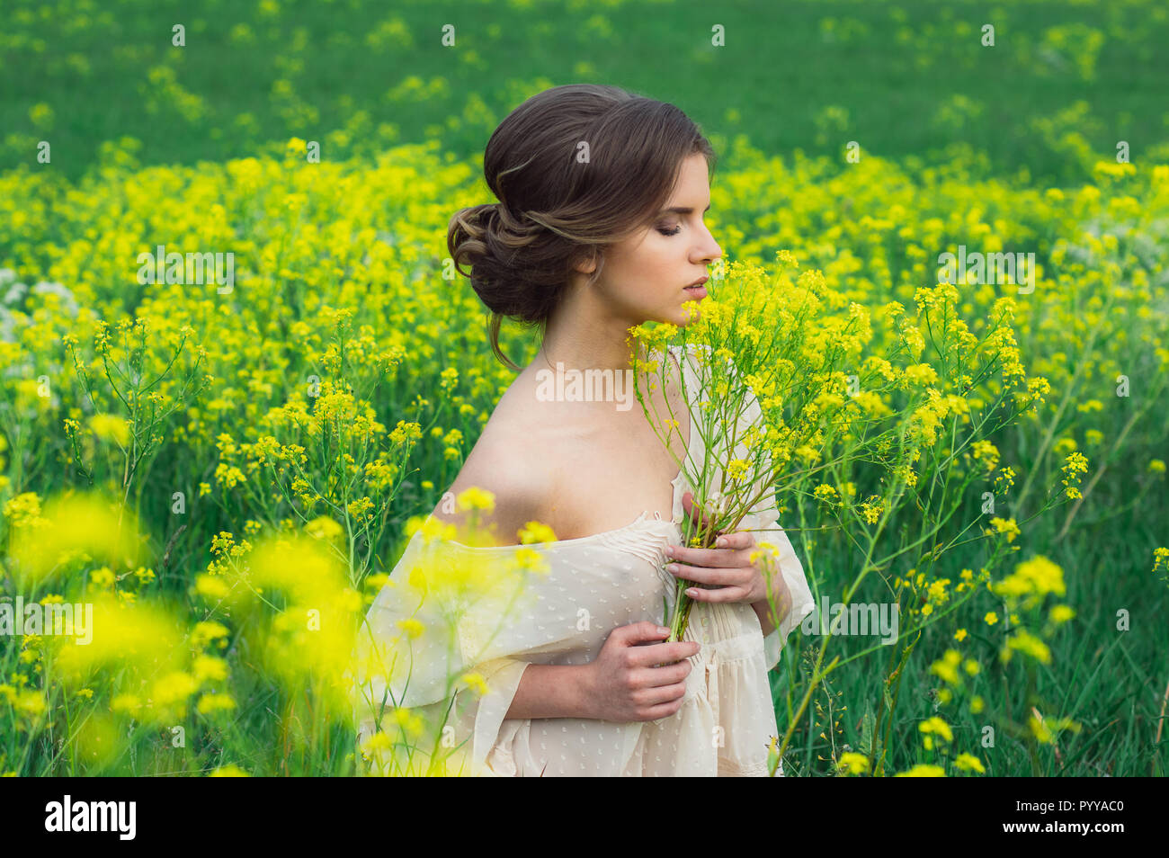 Portrait of young beautiful girl in field with bouquet of yellow ...