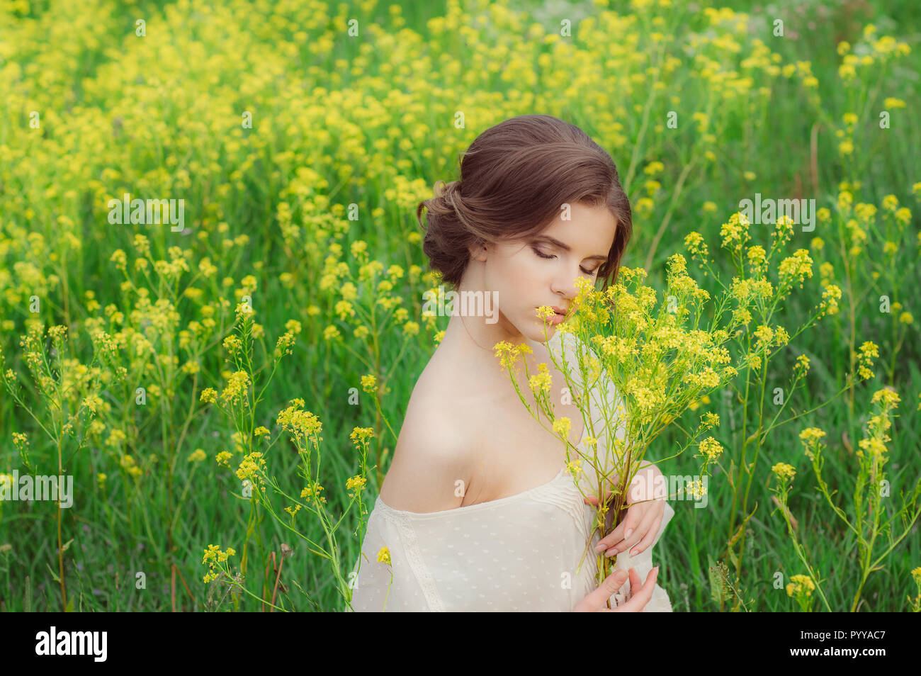 Portrait of young beautiful girl in field with bouquet of yellow flowers in hands with closed eyes Stock Photo