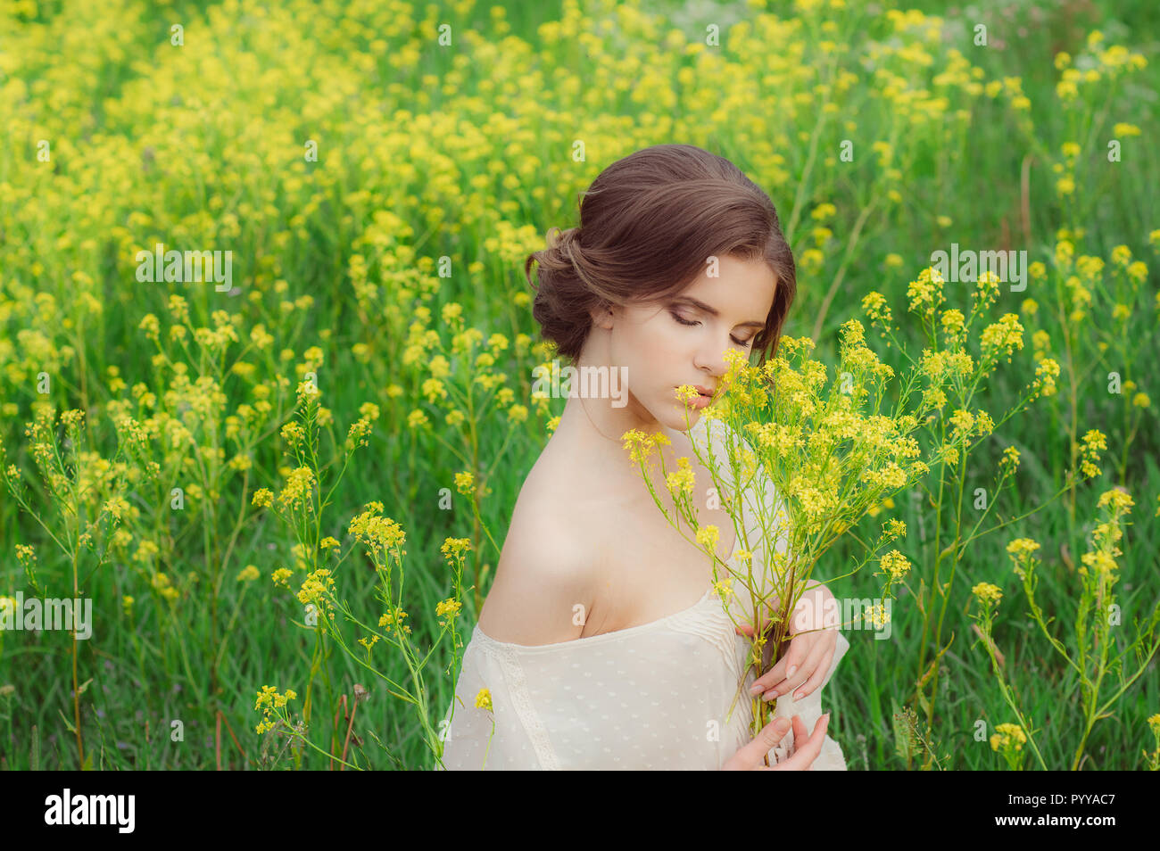 Portrait of young beautiful girl in field with bouquet of yellow ...