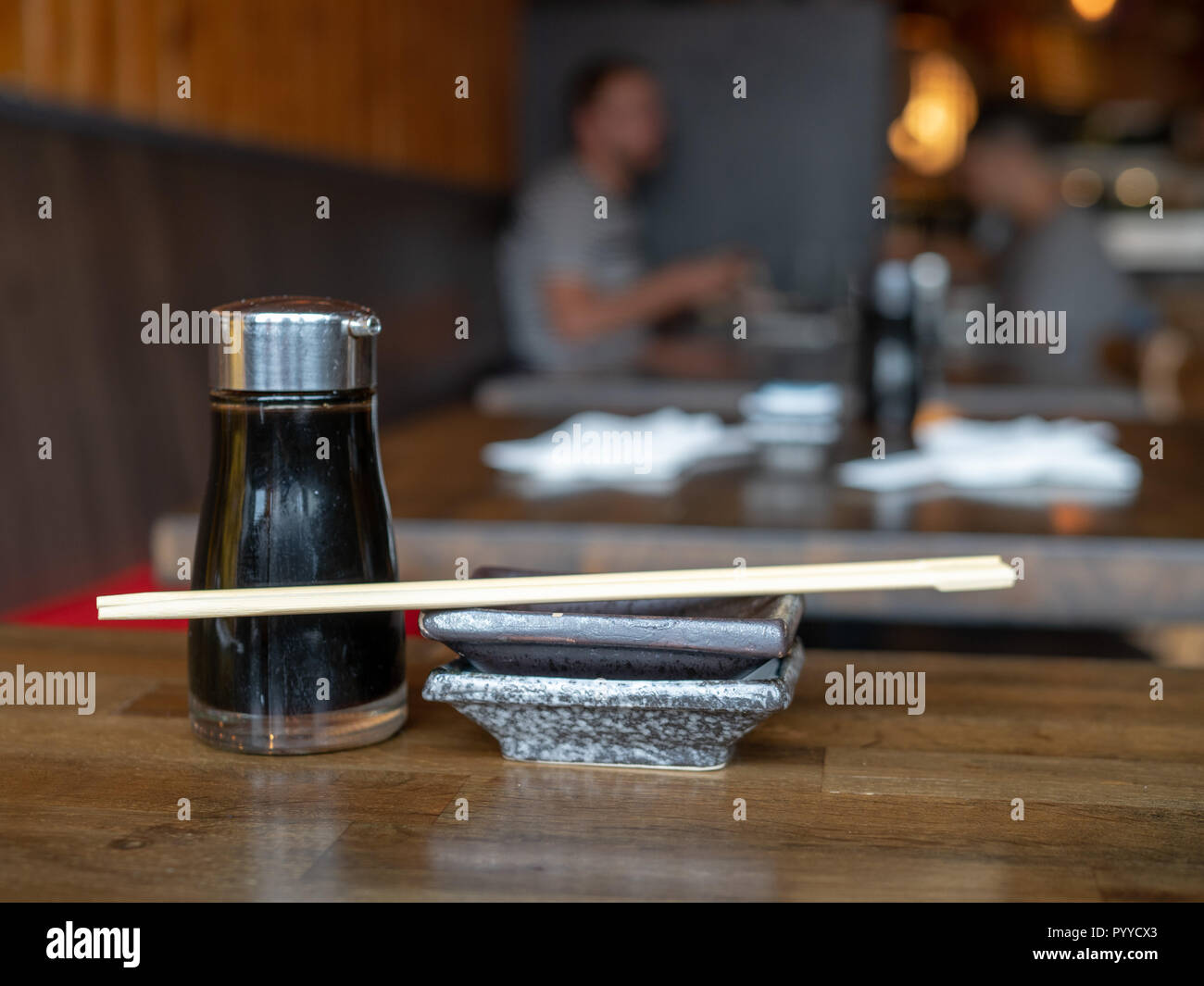 Soy sauce dispenser, dish, and wooden chopsticks in restaurant with