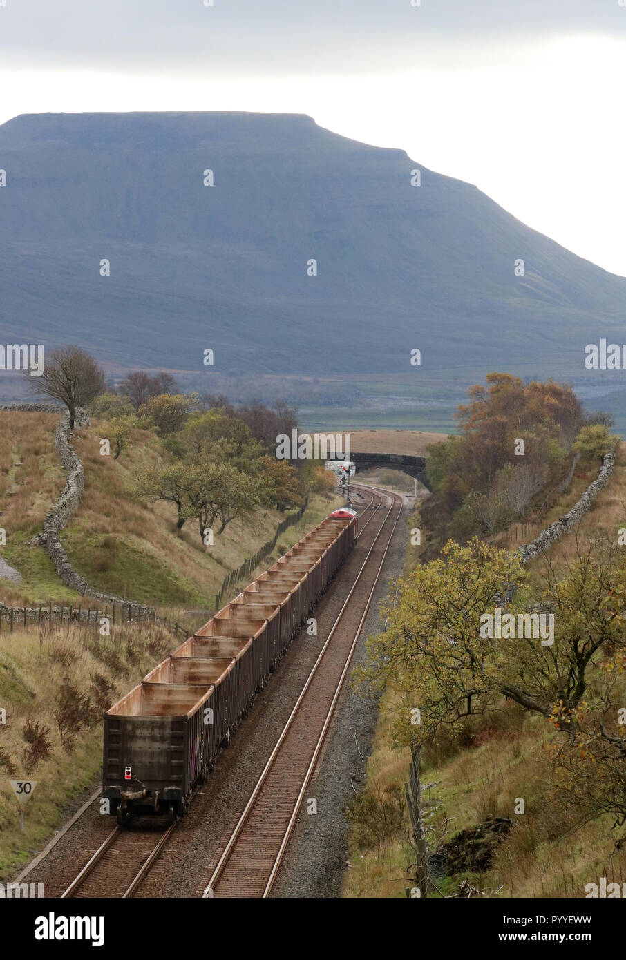 Diesel-electric loco hauling rake of empty wagons on Settle to Carlisle railway line between Blea Moor tunnel and signal box, Ingleborough in distance Stock Photo