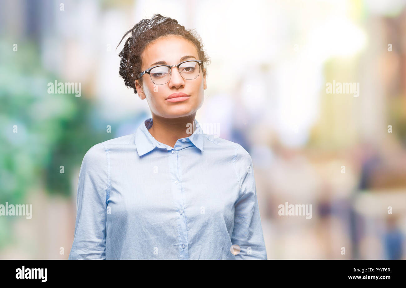 Young braided hair african american business girl wearing glasses over isolated background with serious expression on face. Simple and natural looking Stock Photo