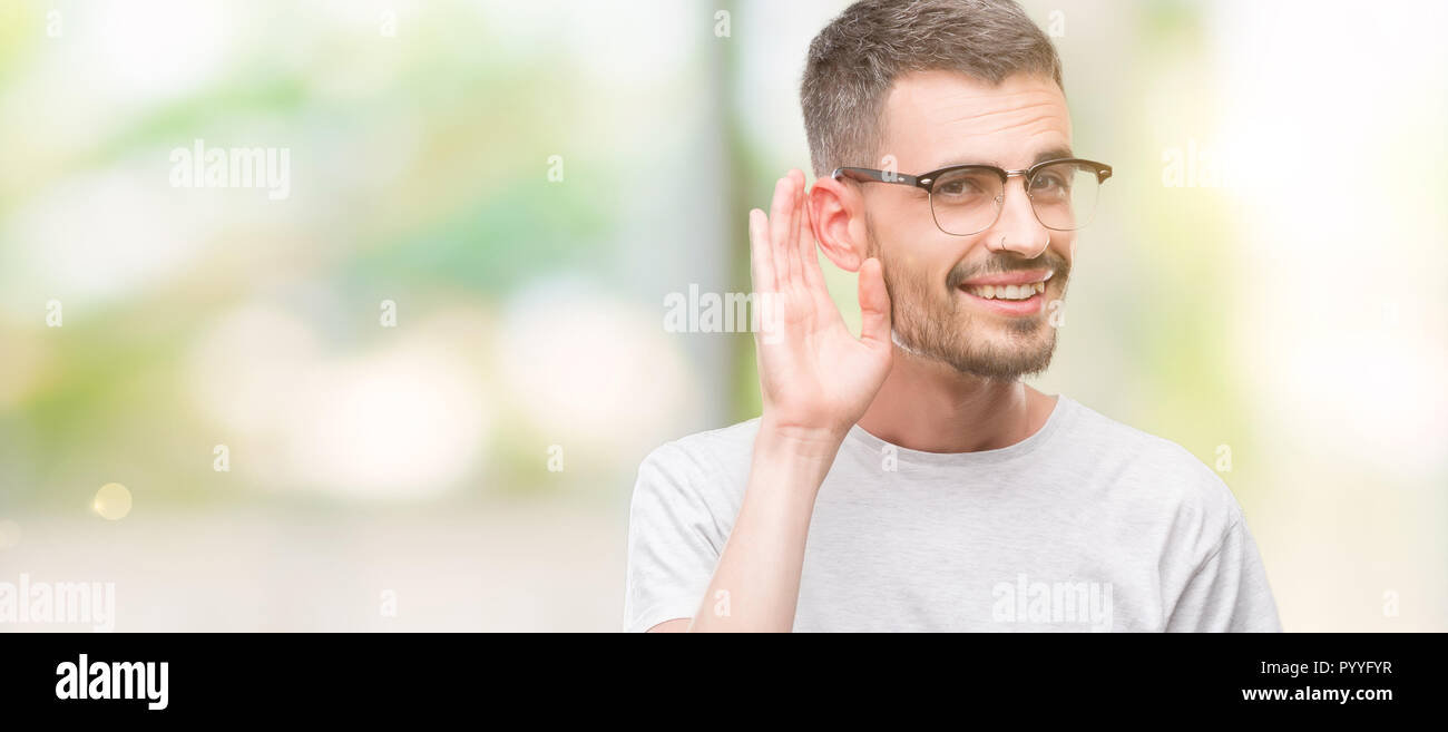 Young tattooed adult man smiling with hand over ear listening an hearing to rumor or gossip. Deafness concept. Stock Photo