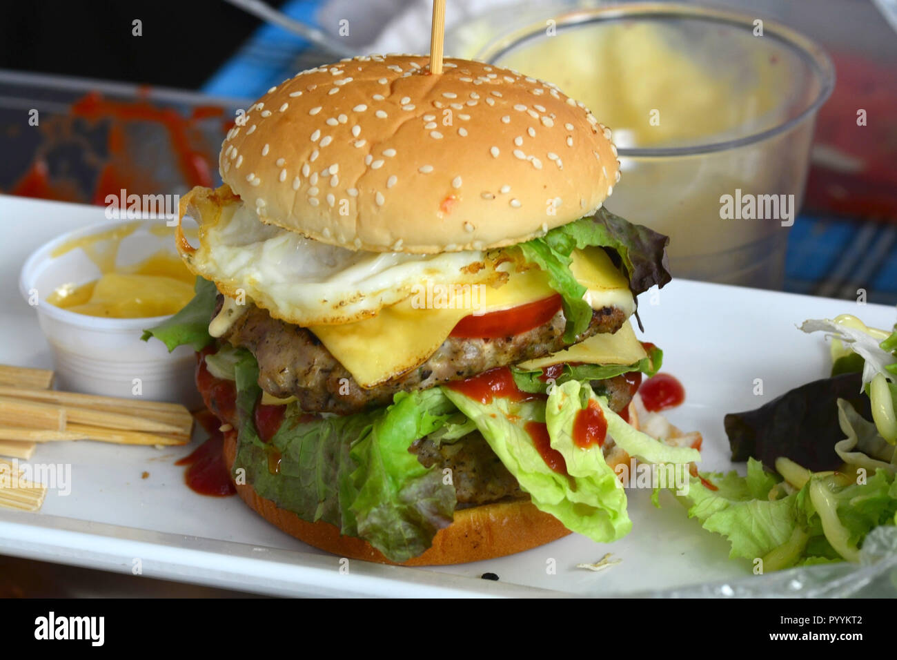 Classic American Burger Stacked High with Lettuce, Tomato, Bacon, Fried Egg Stock Photo