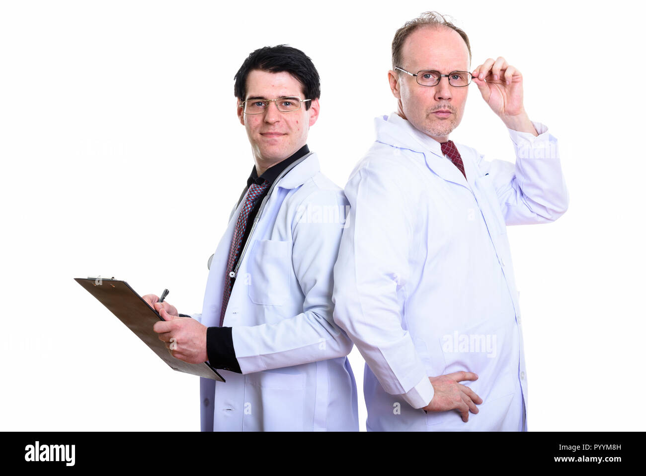 Mature man doctor holding eyeglasses with young man doctor writi Stock Photo