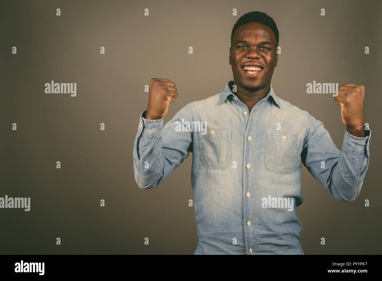 Young happy African man smiling with both arms raised against gr Stock Photo