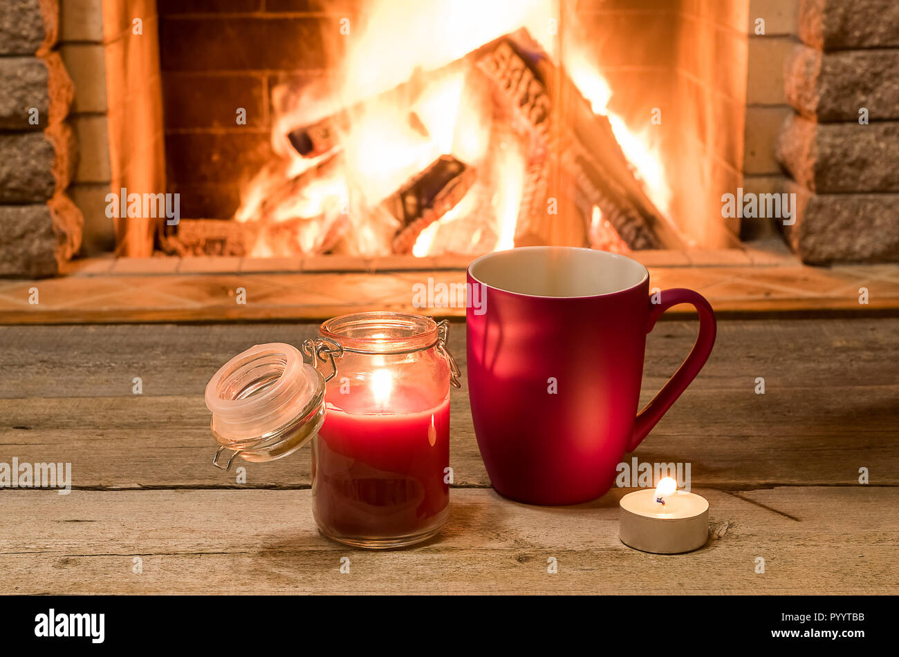 Red cup with hot tea and candles , near cozy fireplace, in country house, winter vacation, horizontal. Stock Photo