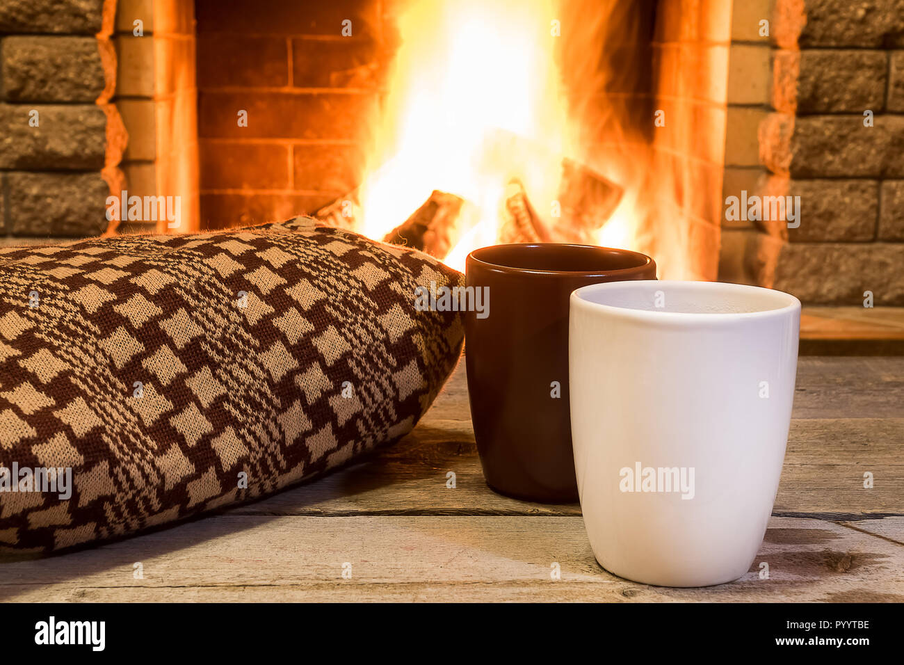 Two cups for hot tea and cozy warm scarf near fireplace, in country house, winter vacation, horizontal. Stock Photo