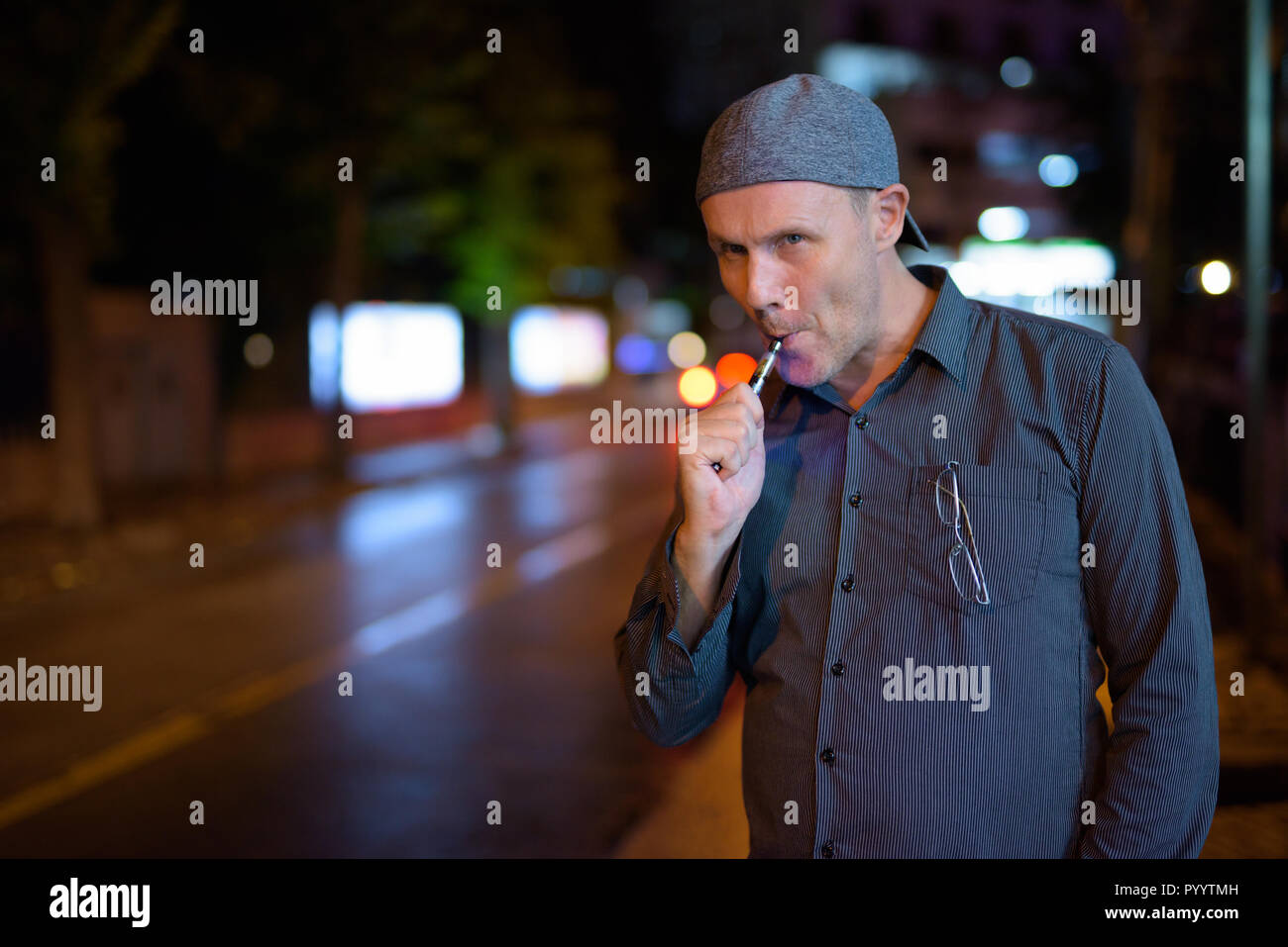 Mature man smoking electronic cigarette in the streets at night Stock Photo