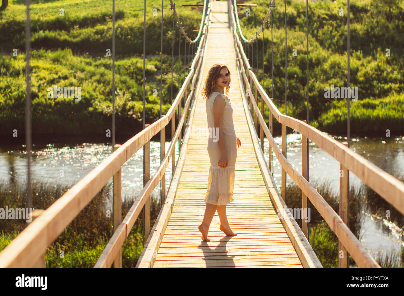 Beautiful girl standing on the center of the wooden bridge across the ...