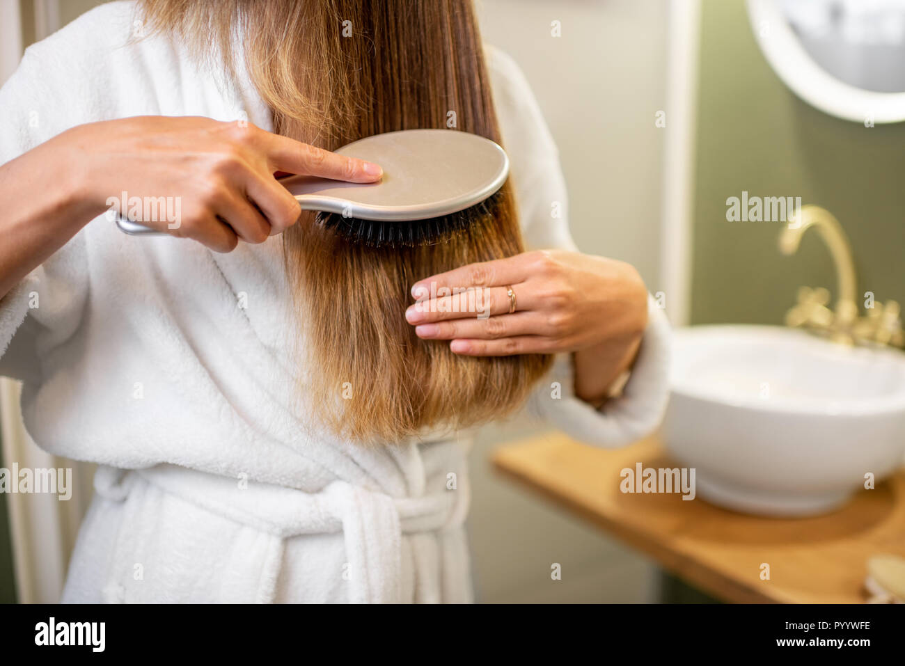 Woman combing hair with brush in the bathroom, close-up view with no face Stock Photo