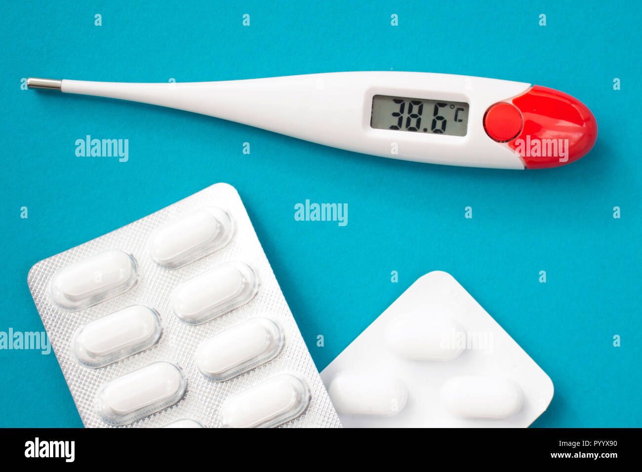 White digital clinical thermometer shows fever heat temperature and pills on blue background