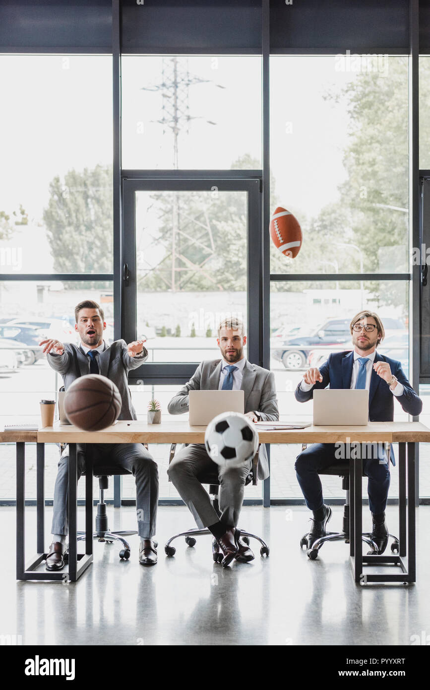 young office workers in formal wear throwing balls while working with laptops in office Stock Photo