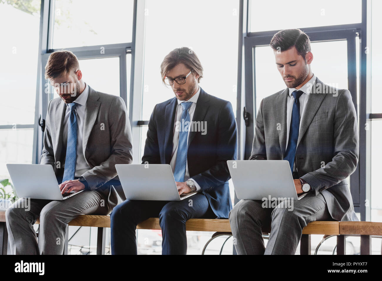 three young businessmen in suits sitting and using laptops Stock Photo