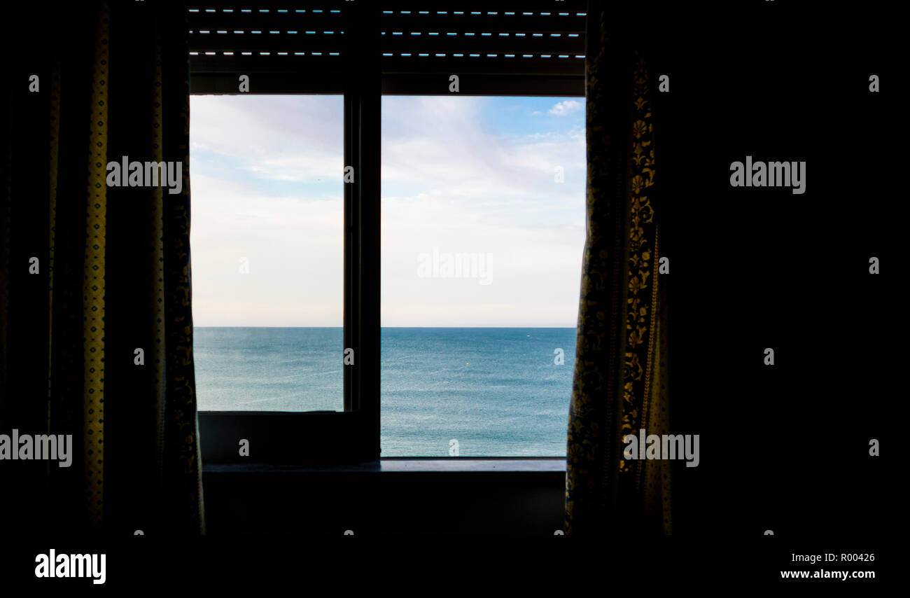 ocean seen through a window with roller blind and curtains Stock Photo