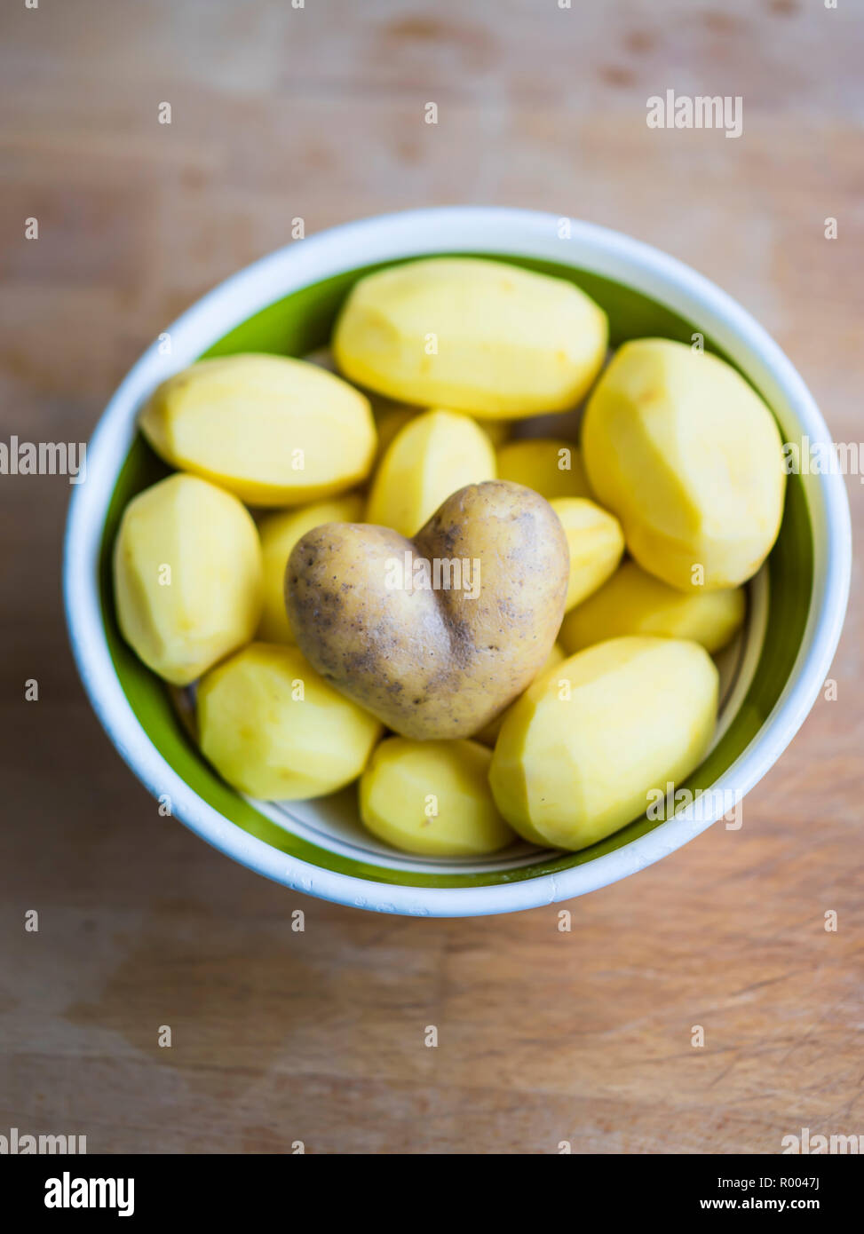 peeled potatoes in a bowl, one unpeeled potato in the shape of a heart Stock Photo