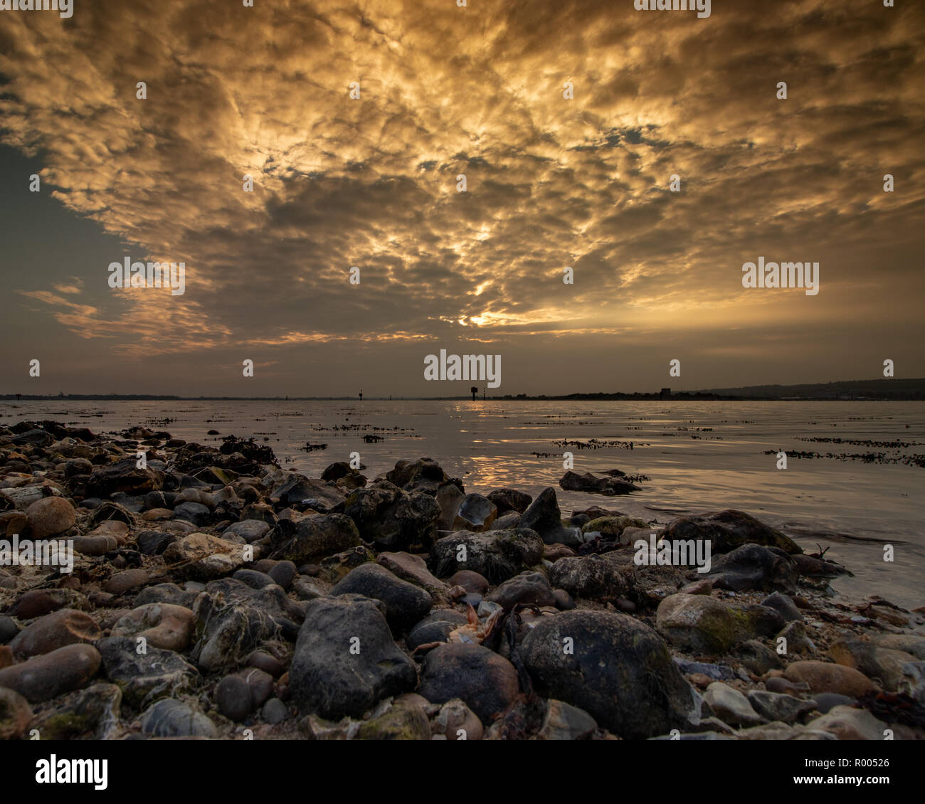 Rocky coastline at sunset with light rays shining through the clouds Stock Photo