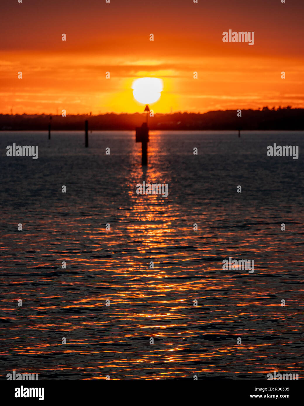 shoreline sunset with Beach marker in in foreground and sun reflection on the waves Stock Photo