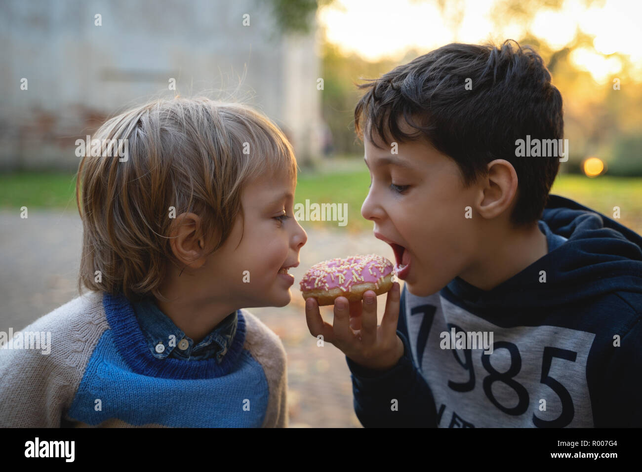 Two caucasian boys eating one donut outdoors closeup. Childhood. Stock Photo