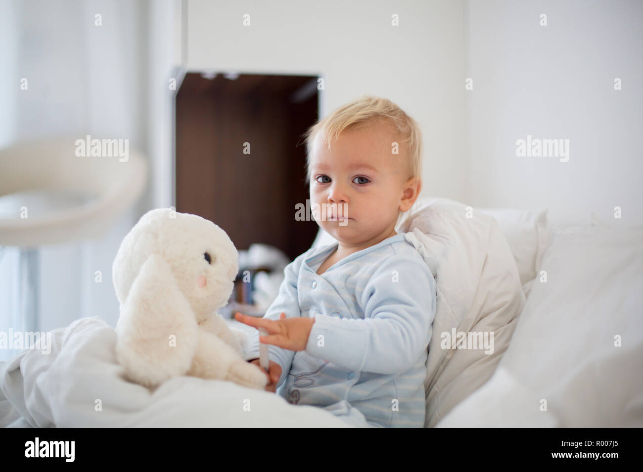 Little toddler boy in pajama with running nose and fever, lying in bed