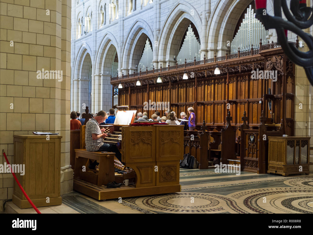 Organist sitting at an Abbey organ looking at his mobile phone choir in the background. Stock Photo
