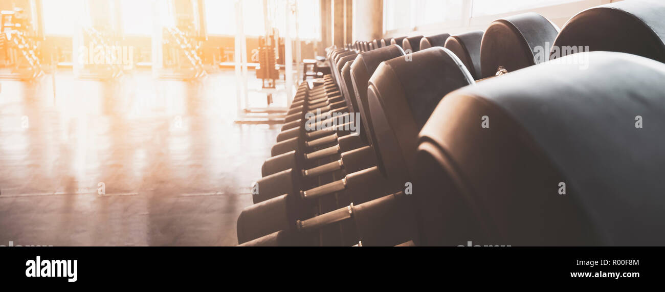 Gym equipment wide interior gym for fitness banner background close up dumbbells and blurred equipment Stock Photo