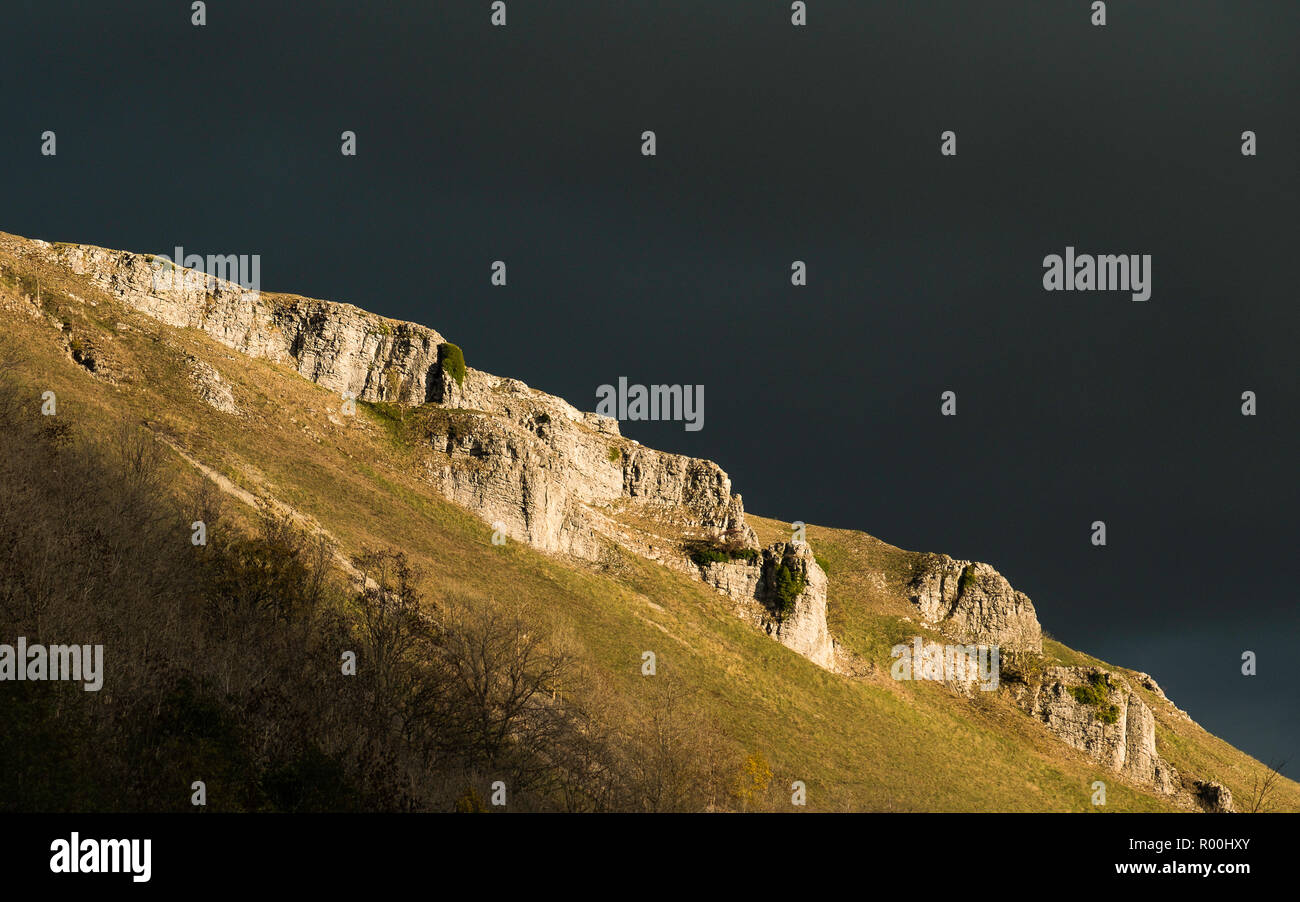 Sunlight picks out the limestone crags in Monsal Dale as a rain cloud passes above. Stock Photo