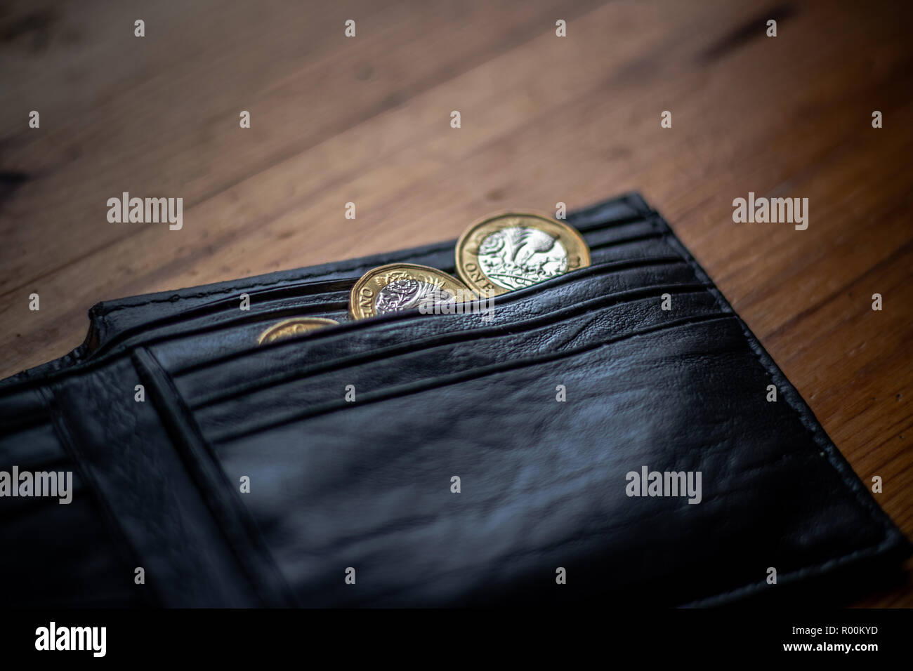 New Great British Pound GBP Coins laying casually on top of black wallet on wooden surface. Wealth, Money, Cash, Change. Stock Photo