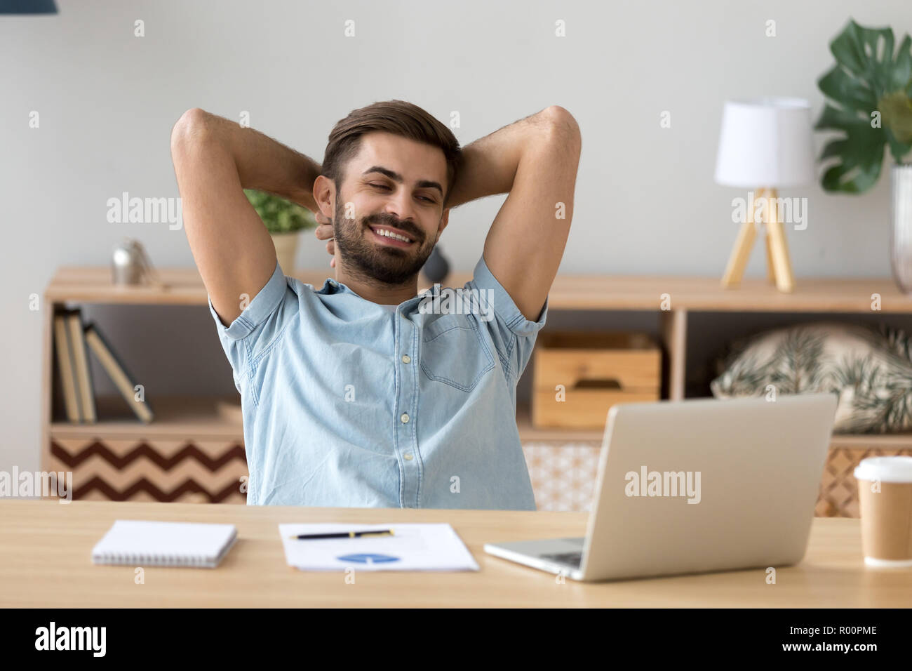 Relaxed man sitting holding hands behind head indoors Stock Photo